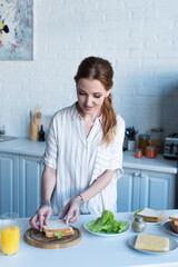 woman preparing sandwich with toast bread, lettuce and cheese