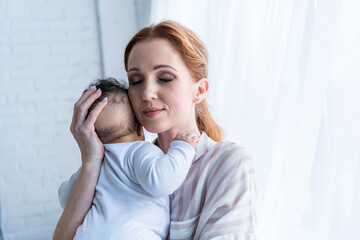 happy woman holding infant african american daughter with closed eyes