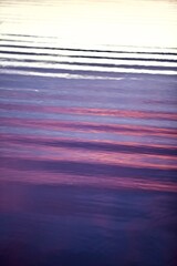 High-contrast shadows and bright reflections on the glowing purple and magenta surface close-up. Bright ripples, abstract pattern on colorful water surface. Abstract backgrounds and textures. 