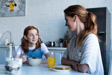 happy redhead girl talking to smiling mother during breakfast
