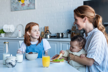 Obraz na płótnie Canvas happy woman having breakfast with multiethnic daughters in kitchen