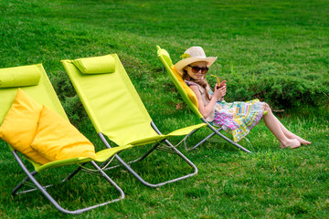 Cute girl relaxes with juice at chair on grass. Outdoor photo. Concept of relaxation and vacation.