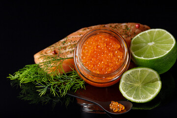 Red  salmon trout caviar in a glass  jar  and in spoon with fresh fish steak, lime and dill