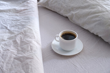 White cup of black coffee in a white bed.