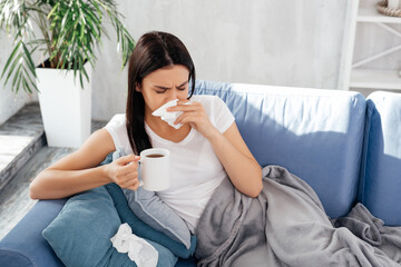 Young diseased female drinking tea on sofa