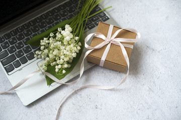 laptop, bouquet of lilies of the valley, gift box on gray background. colleague's congratulations. a gift to your girlfriend.