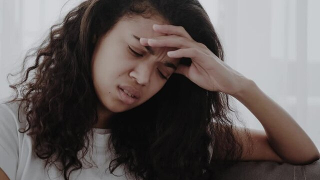 African young woman sit on couch frown face expressions touches temples reduces sharp severe migraine or headache feeling discomfort unpleasant sensations caused by weather changes or hangover concept