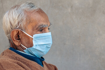 Side face portrait of old Indian man wearing protective mask during corona virus pandemic in 2021. Concept of geriatric care. With copy space in background