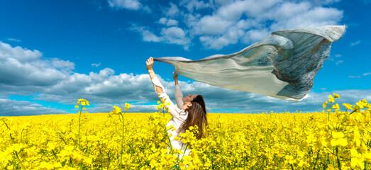 Beautiful woman with wind fluttering scarf in the rapeseed field. Woman freedom. Women rights topic.