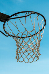 A basketball basket hangs on a large black hoop against a blue sky