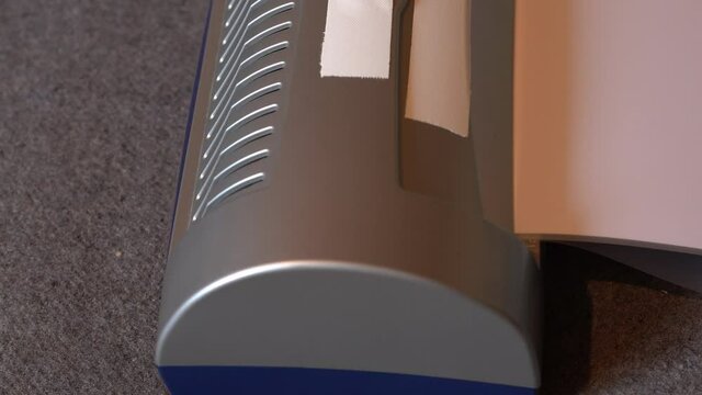 Laminated white paper slides out of the laminator