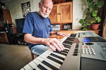 Senior man playing a synthesizer in his home environment. Wide angle view