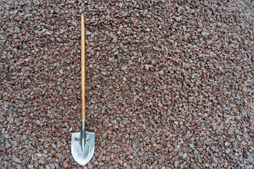 An old shovel with a wooden handle lies on a plane covered with pink granite rubble. Background....