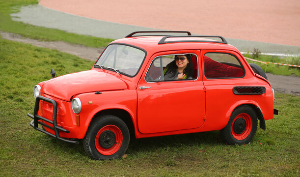 Young woman posing in a bright red retro Zaporozhets car