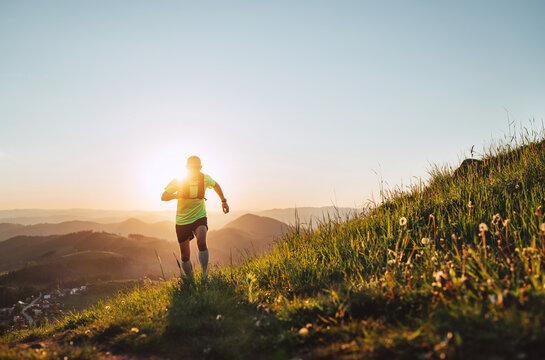 Active mountain trail runner dressed bright t-shirt with backpack in sport sunglasses running endurance marathon race by picturesque hills at sunset time. Sporty active people backlight concept image.
