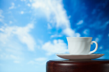 White cup of coffee or tea with steam on a wooden table on a background of blue sky