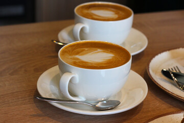Two cups of aromatic coffee, cappuccino with latte art on a wooden table. Beautiful foam, white ceramic cups.