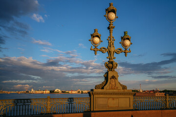 Fototapeta premium Trinity Bridge lantern and view of the spit of Vasilievsky Island and the Peter and Paul Fortress in the background in the first rays of the sun, St. Petersburg, Russia