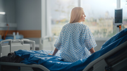 Hospital Ward: Beautiful Caucasian Female Patient Sitting on a Bed, Fully Recovering after...