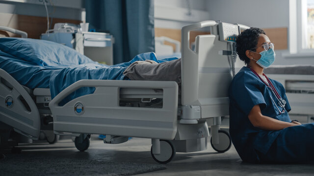 Hospital Intensive Care Coronavirus Ward: Portrait Of Sad, Tired Black Nurse Wearing Face Mask Sitting On A Floor, Sorry For All The Patients Lost To Pandemic. Brave Hero Paramedics Save Lives