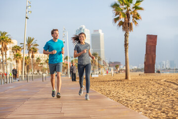 Obraz premium Running interracial couple friends talking while training together on morning beach run exercise. Fitness people runners, Barcelona Beach. Multiracial athletes jogging. Sport summer active lifestyle.