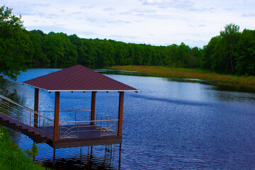 Wooden gazebo on the shore of a picturesque lake on a summer evening