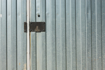 Fragment of a silver metal fence with a door. There is a black lock bar with a closed keyhole. Background. Texture.