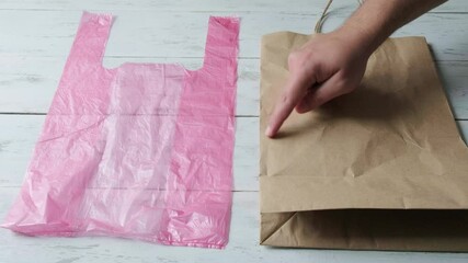 Male hand points with a finger to choose between a plastic bag and a paper bag. Stopping on paper raises his thumb up. Concept of a day without a plastic bag.