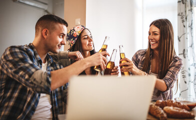 Group of young students at the home party.They watching online stream and making fun.Toasting with beer.
