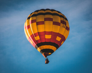 Fototapeta premium yellow and red hot air balloon with black details flying over a blue sky