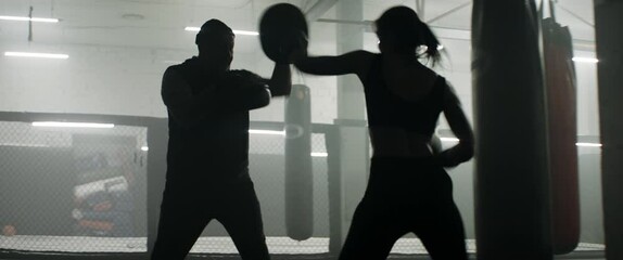 HANDHELD WIDE to CU Caucasian female boxer practicing with her trainer in a boxing gym, preparing for a fight. Shot with 2x anamorphic lens