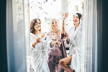 Pretty young women friends in bathrobes and pajama clink elegant glasses with delicious champagne...