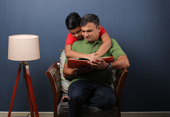 Father's day concept - Happy indian father reading book with his son in living room.