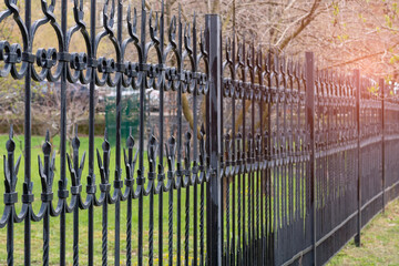 Black figure metal fence against park with green grass. Selective focus.