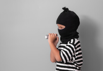 little boy in thief outfit with flashlight against a gray background.