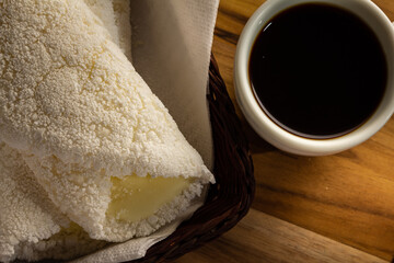 Duas tapiocas dentro de uma pequena cesta de vime e uma xícara de café sobre mesa de madeira.