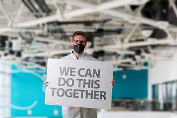 human in mask holding a white frame banner with text 