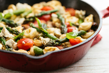 Cast iron pan with vegetable tortellini with asparagus, tomatoes, mushrooms and home made vegan feta cheese