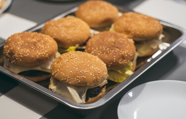 Homemade burgers with sesame bun, on metal tray on table