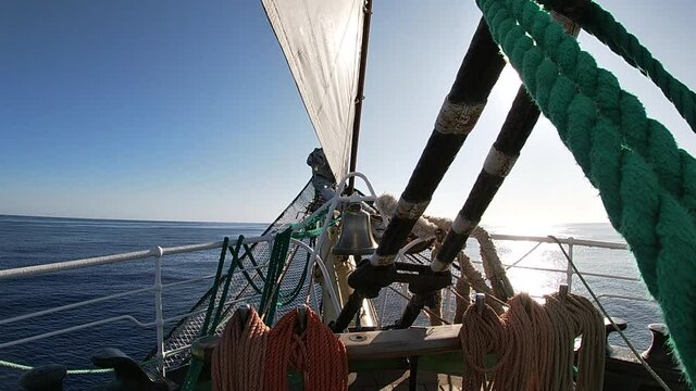 Sunny ocean view from the bow of the sailing ship. Sail, ropes and bell on the deck.