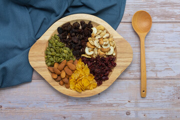 Grains in wooden circle tray, Currant,Cashew nut ,Almond,Pumpkin seed,Cranberry dried fruit, And Cornflakes on wooden floor background.