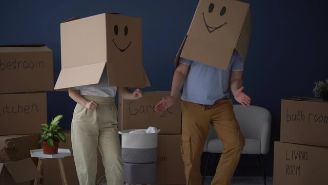 Moving and relocation concept. Packing and decluttering. Unrecognizable couple, husband and wife, dancing with cardboard boxes on their heads, funny video