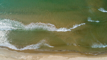 Aerial view of turquoise ocean wave reaching the coastline