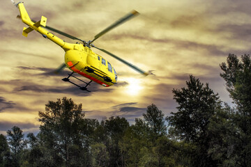 A yellow helicopter is taking-off on background of bright sunset.