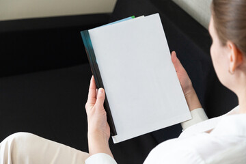 Woman holding brochure with blank cover on wooden background, top view. Mock up for design