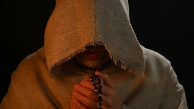 Monk in haircloth cowl robe praying in candlelight