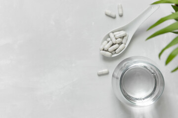 Collagen pills in a spoon and a glass of water on a gray background with a copy space. Extra protein intake