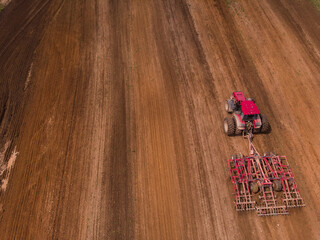 A tractor with a disc harrow plows a field for sowing. Aerial photography.