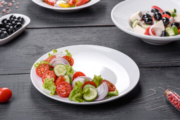 Fresh delicious salad with vegetables: tomato, cucumber, onions and greens with olive oil