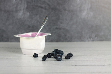 a plastic bowl of blueberry yoghurt and a pile of berries on wooden background